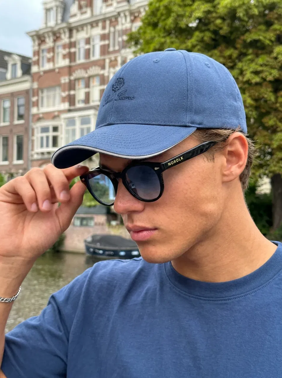 Man met blauwe cap en NORDLK zonnebril bij een gracht